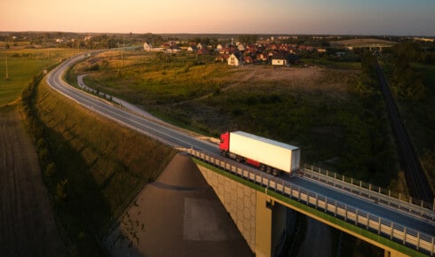 Was ist HVO100: Luftaufnahme eines Lastwagens auf einer Landstra&szlig;e bei Sonnenuntergang, mit einem Dorf und einer Br&uuml;cke in einer nordischen Landschaft &ndash; sinnbildlich f&uuml;r einen Fuhrpark, der mit erneuerbarem Diesel f&auml;hrt