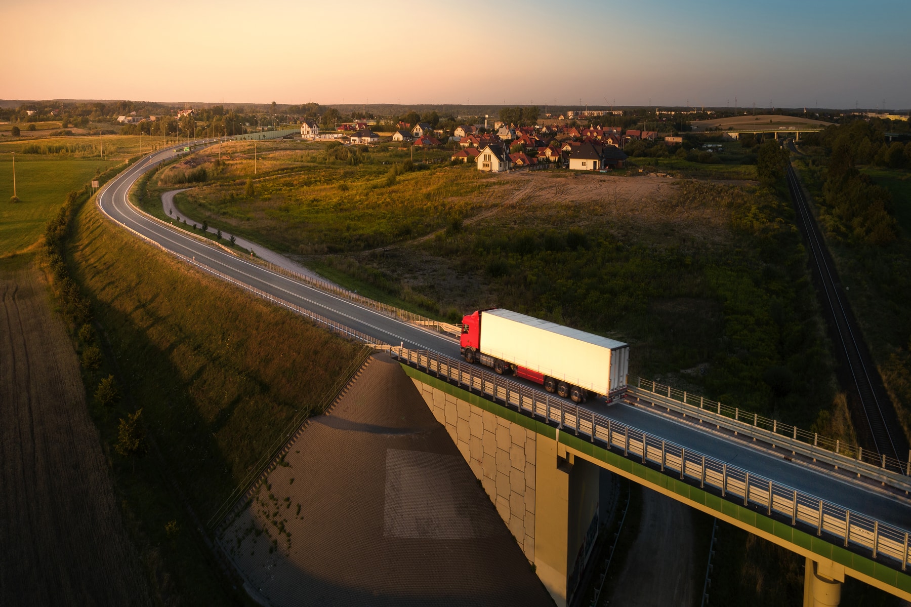 Was ist HVO100: Luftaufnahme eines Lastwagens auf einer Landstraße bei Sonnenuntergang, mit einem Dorf und einer Brücke in einer nordischen Landschaft – sinnbildlich für einen Fuhrpark, der mit erneuerbarem Diesel fährt